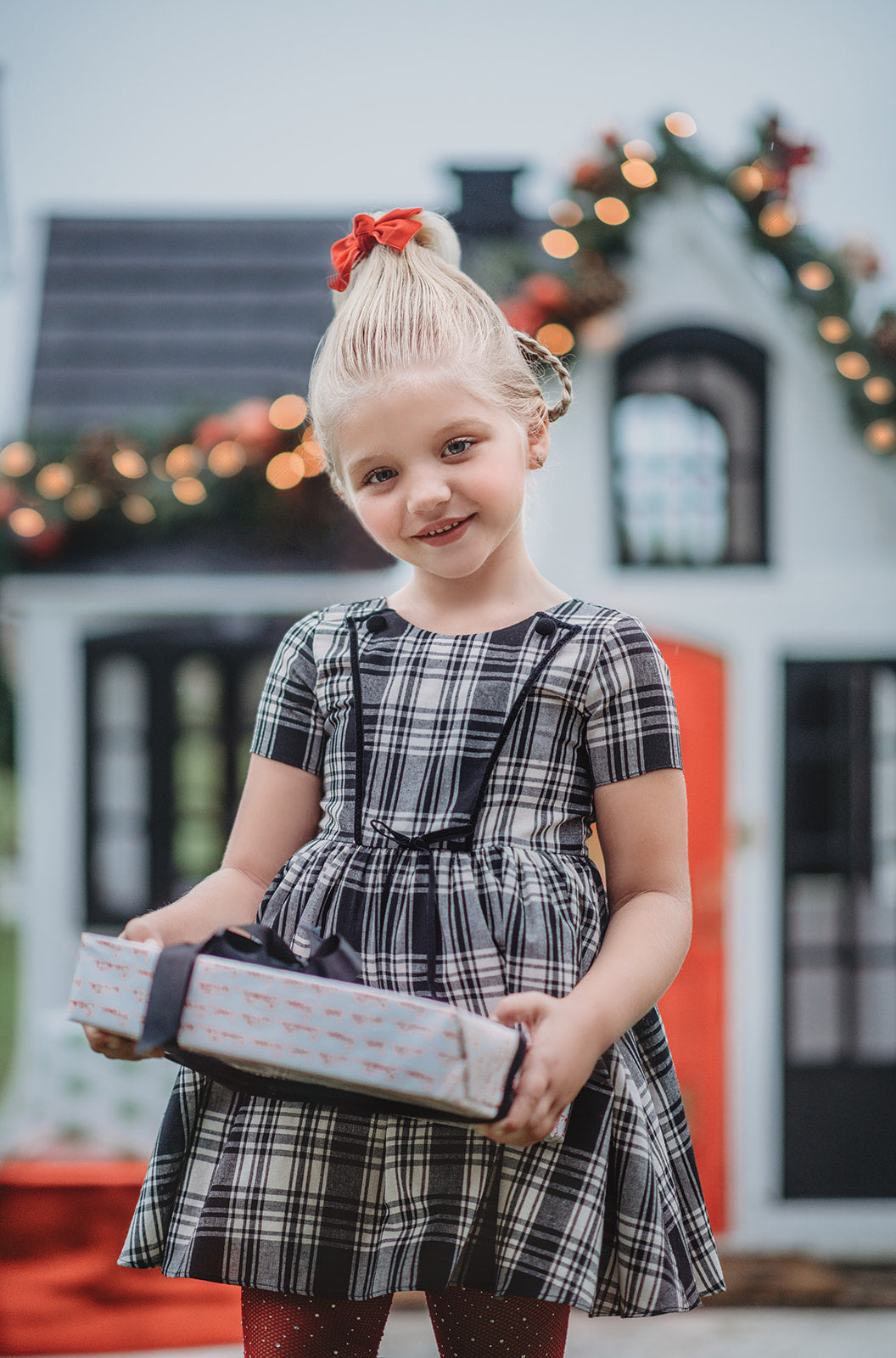 A young girl stands dressed in a black and white vintage plaid dress.  The dress is mid thigh length and a sewn in pettiskirt add fullness to the bottom of the dress. 