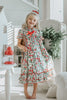 A young child with curly blonde hair stands barefoot on a soft carpet, holding an open book. The child wears *The Original Clara Nutcracker Gown in Winterberry* and reads intently. A decorated Christmas tree is visible in the background, part of our exclusive Christmas Lounge Collection.